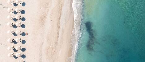An aerial view of a beach with rows of umbrellas and lounge chairs, indicating a resort setting.