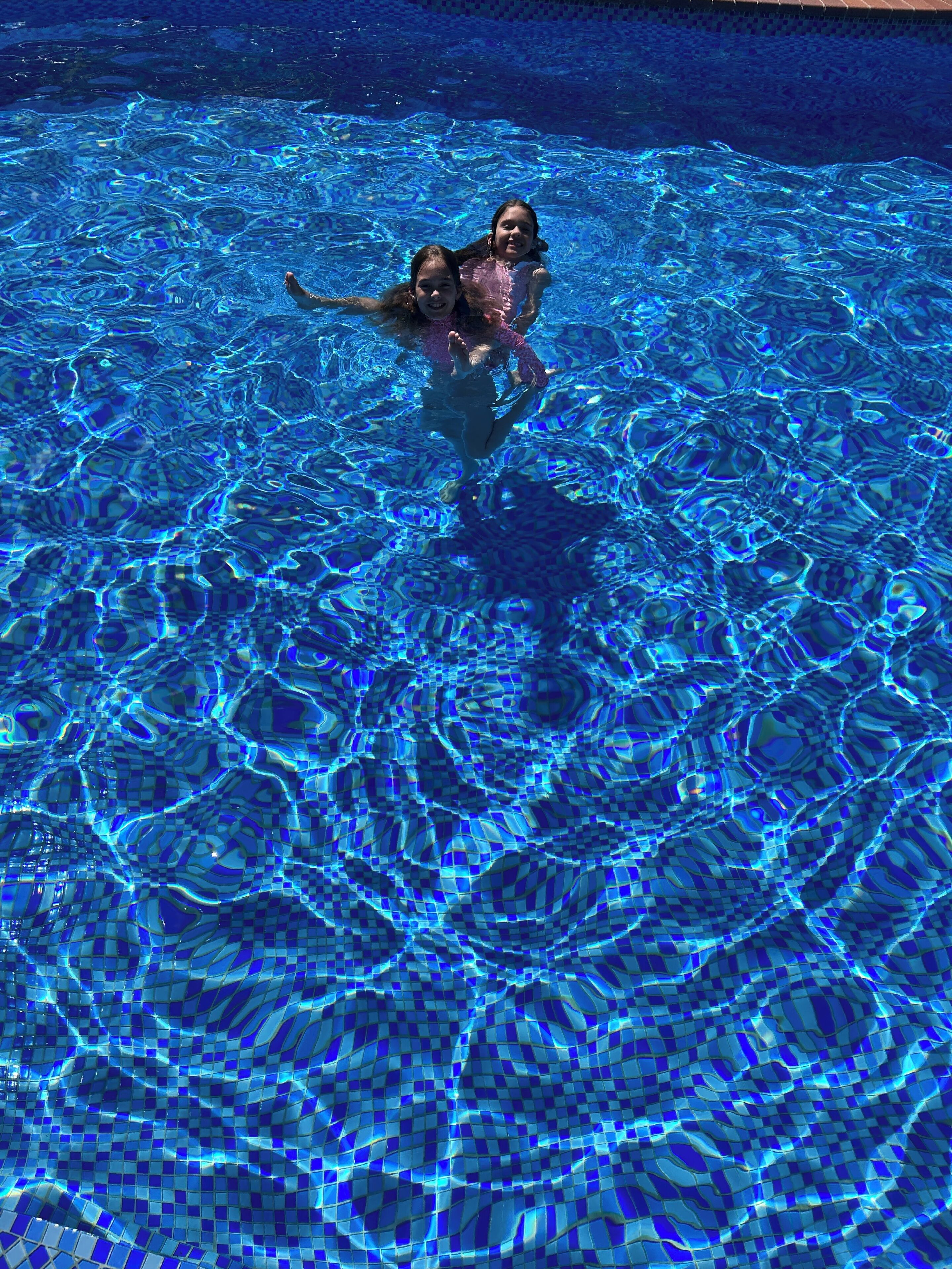 A swimming pool with clear blue water and a tiled bottom.