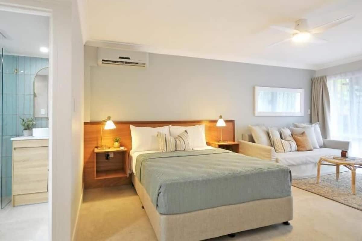 A hotel room with a bed, bedside tables, a sofa, a small table, and a window.