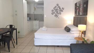 A compact hotel room with a bed, bedside lamp, and a small table with a lamp.