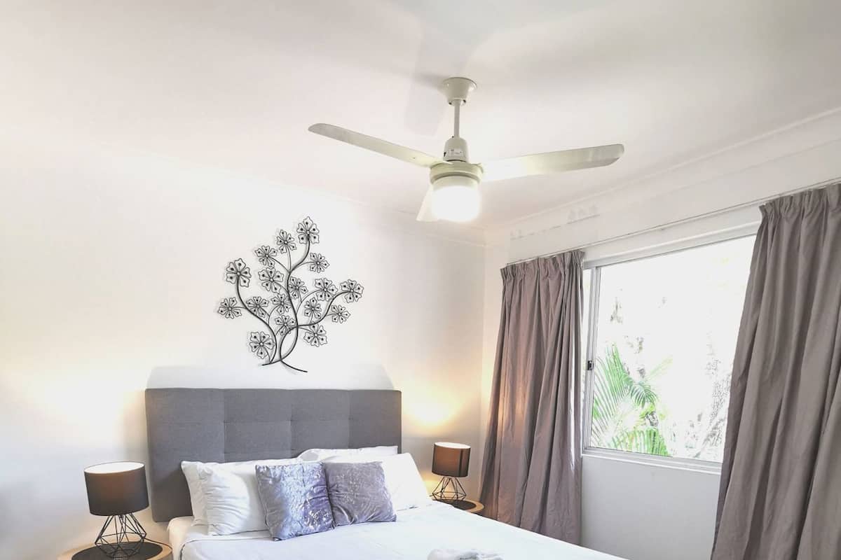 A neatly made bed with a white duvet, a grey headboard, and a ceiling fan.