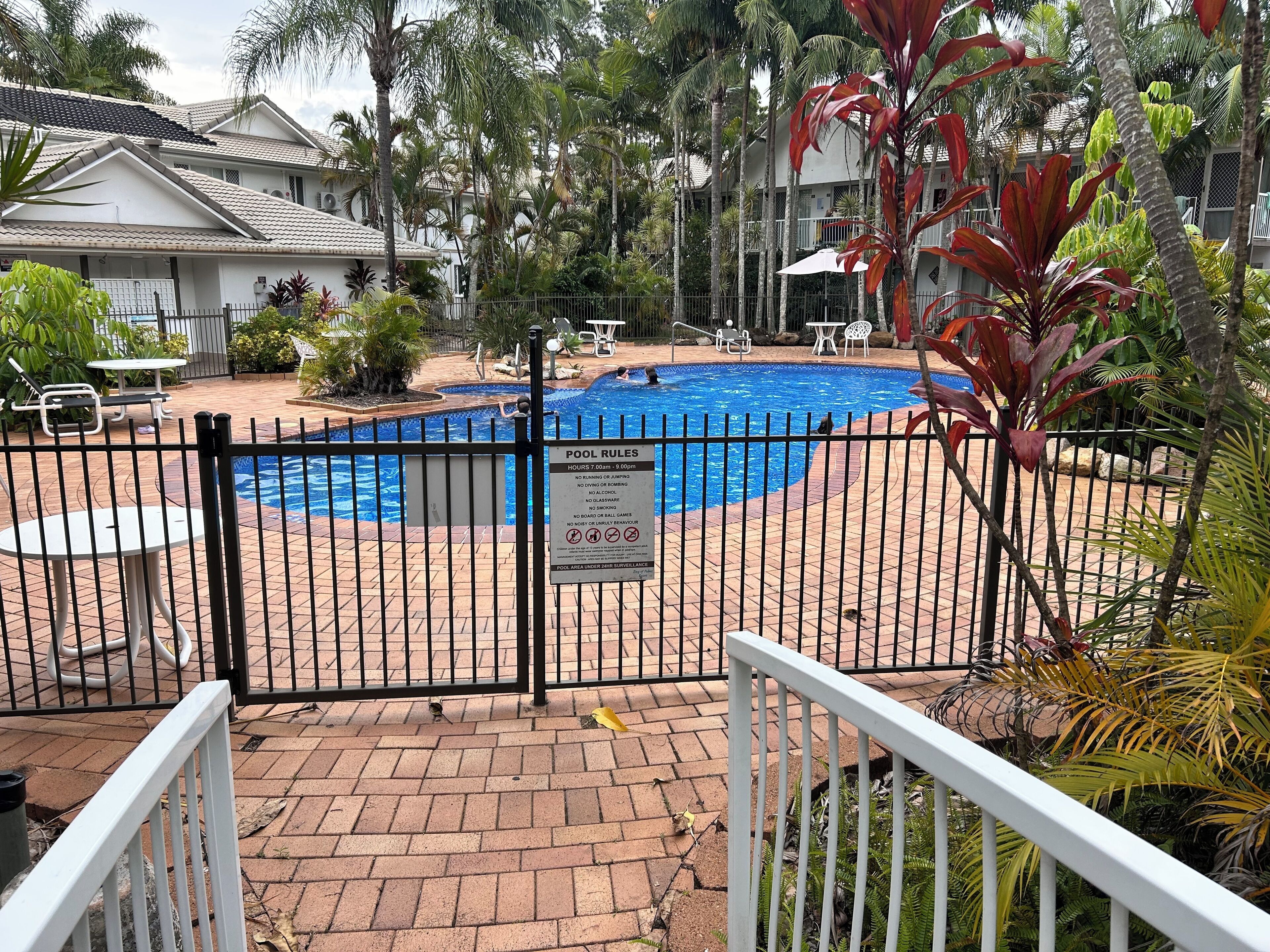 Una piscina rodeada por una valla, con un letrero que indica las normas de la piscina.