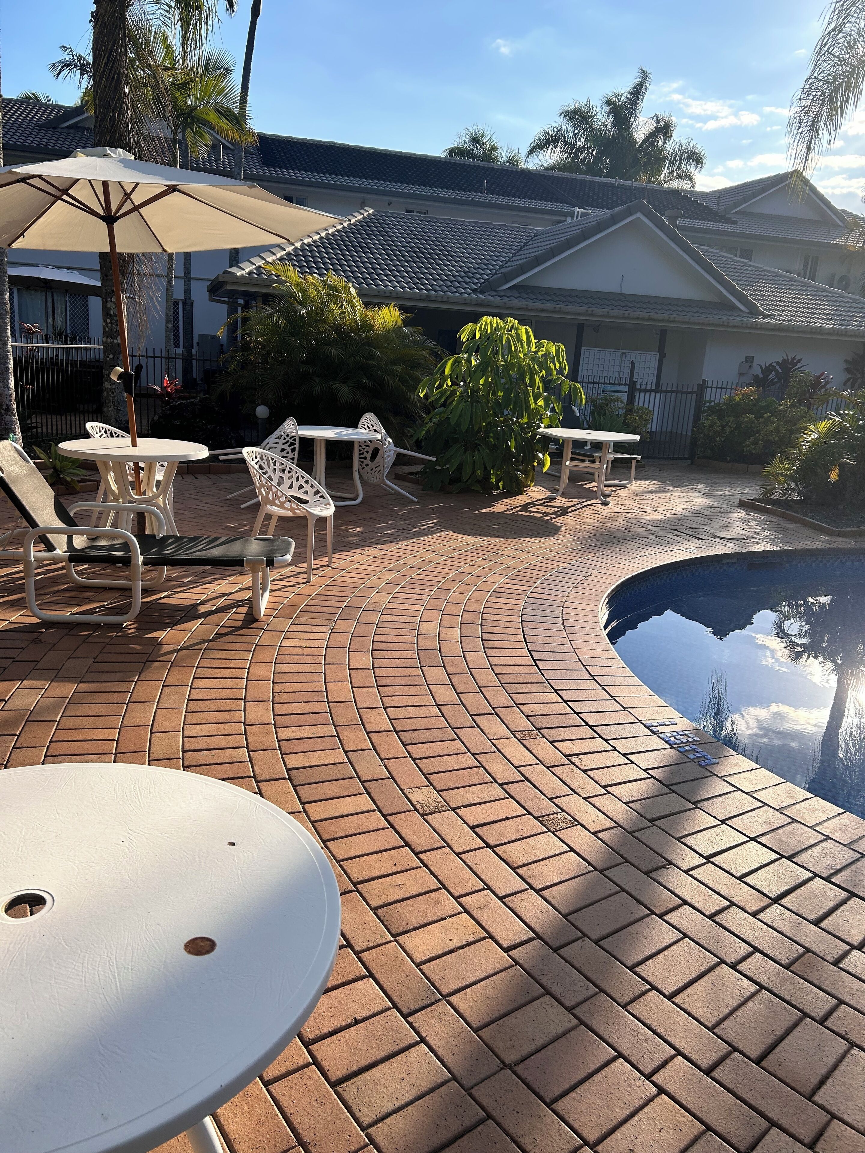 A poolside area with tiled flooring, white outdoor furniture, and a swimming pool.