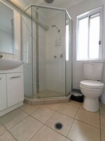 Un baño moderno con ducha envuelta en vidrio, inodoro blanco y lavabo con espejo.