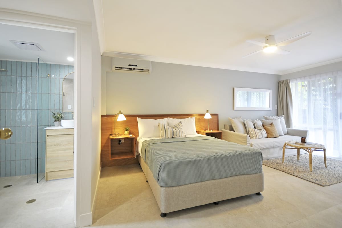 A modern bedroom with a large bed, bedside tables, a nightstand, a ceiling fan, and a view of the bathroom.