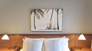 A neatly made bed with two pillows, flanked by two bedside tables with lamps, and a framed picture of palm trees on the wall. - Bay of Palms (Elanora)