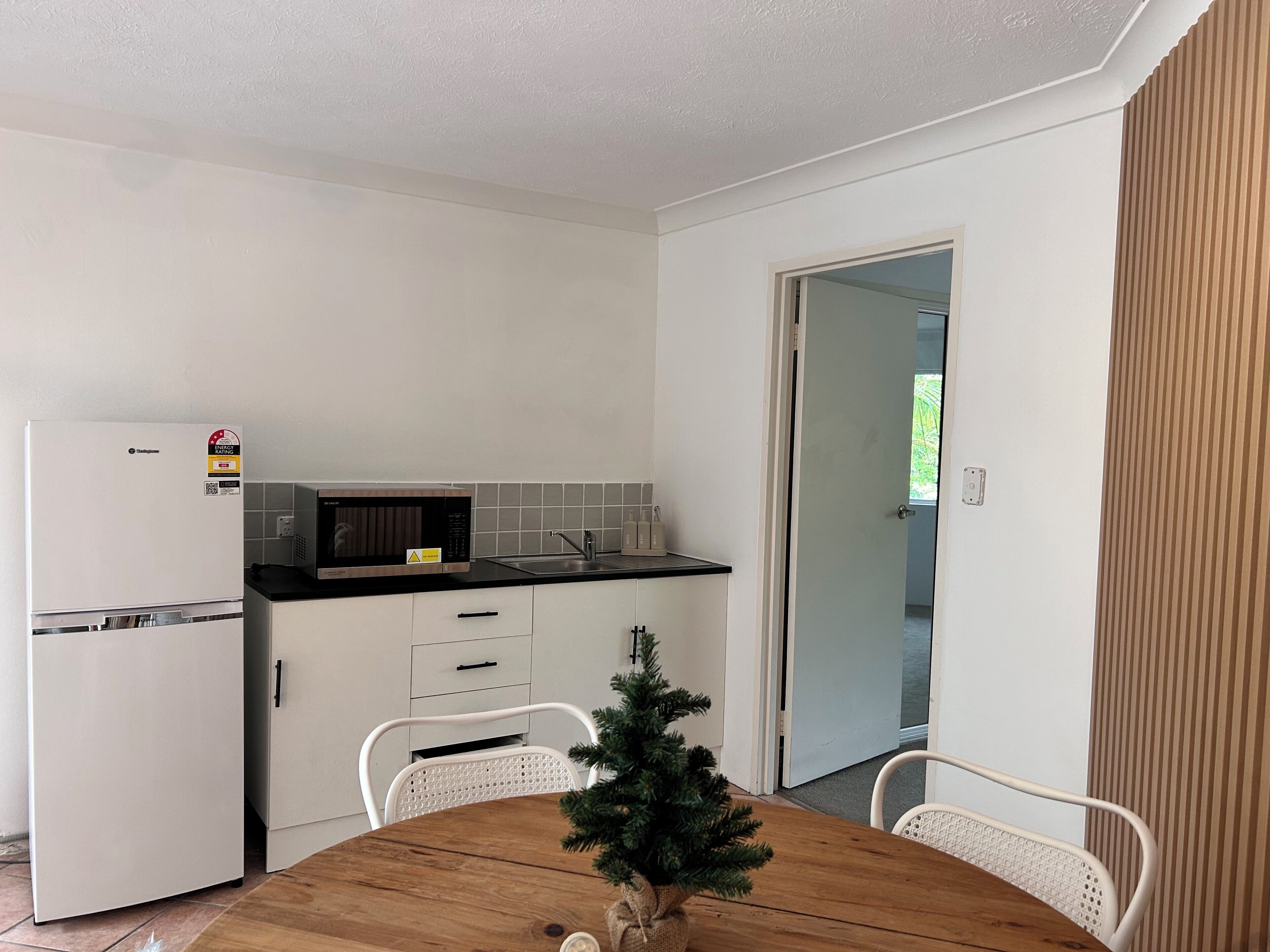 Cocina compacta con refrigerador, microondas y pileta. Hay una pequeña mesa de comedor con sillas y un árbol de Navidad.