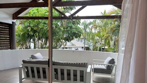 A balcony with a white bench and a glass table, surrounded by lush greenery and a white building in the background. - Bay of Palms (Elanora)