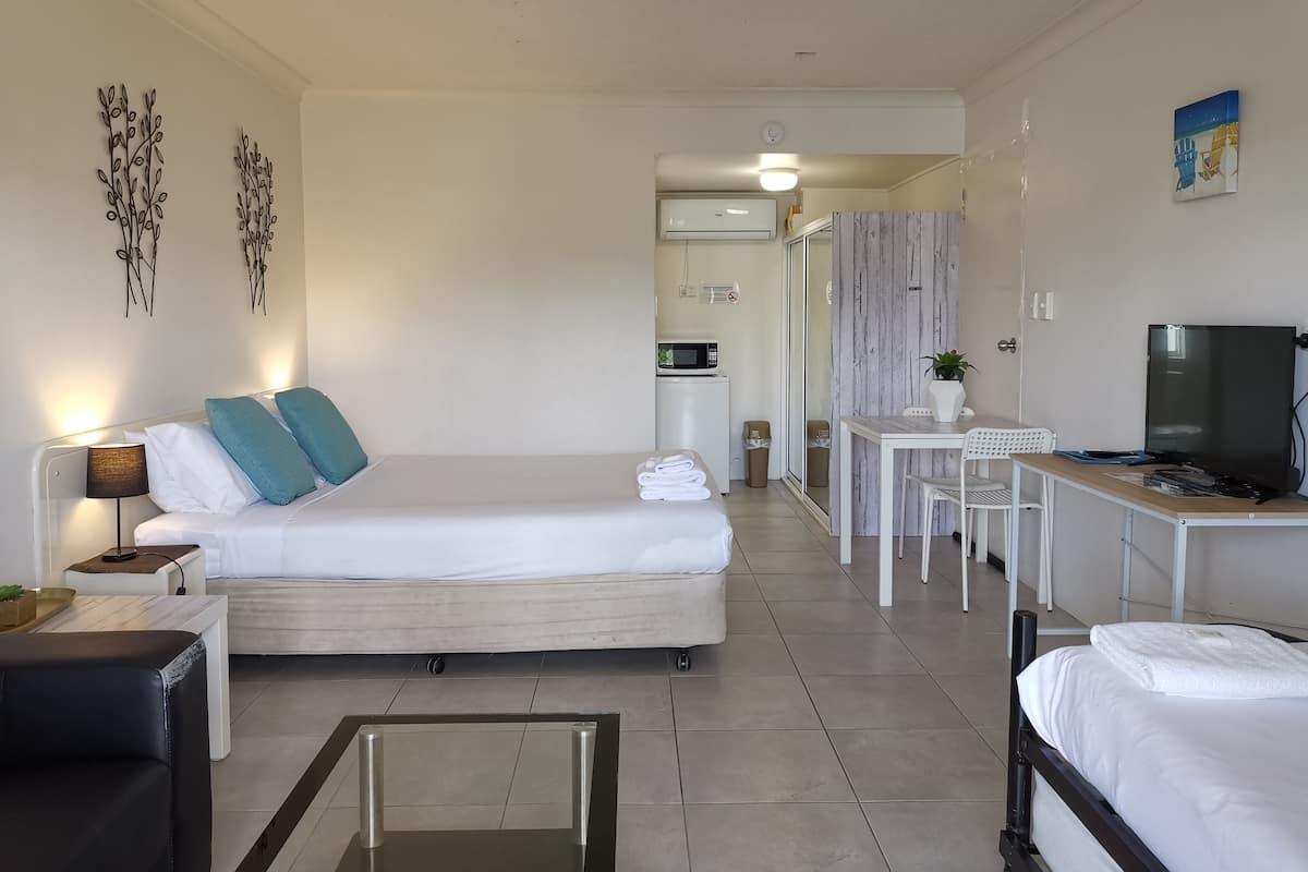 A modern hotel room with a bed, a desk, a TV, and a small seating area.