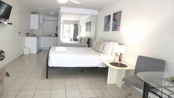 A compact hotel room with a bed, bedside table, chair, and a small kitchenette.