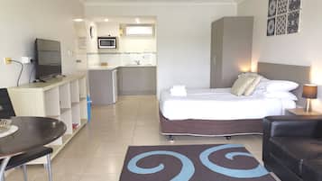 Une chambre d’hôtel équipée d’un lit, d’un bureau, d’une chaise, d’une télévision, d’un four à micro-ondes, d’un lavabo et d’un petit coin cuisine.