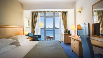Een hotelkamer met een bed, een bureau, een stoel, een dressoir en een groot raam met gordijnen.