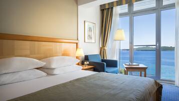 A hotel room with a large bed, a desk, a chair, and a view of the sea.