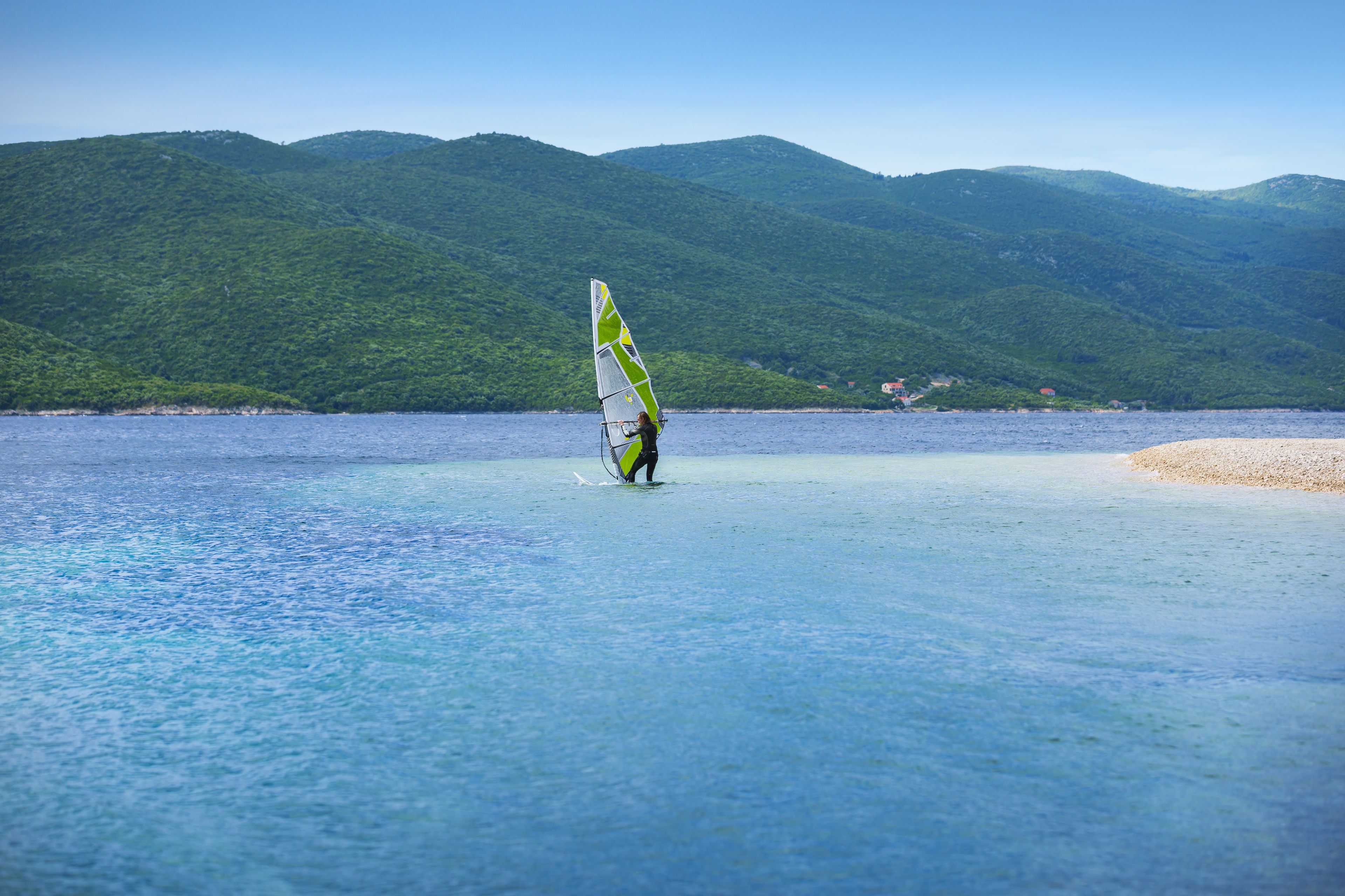 A person windsurfing in a calm sea with a mountainous backdrop.