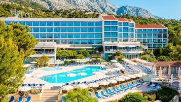 A hotel with a large pool area, multiple lounge chairs, and a mountainous backdrop.