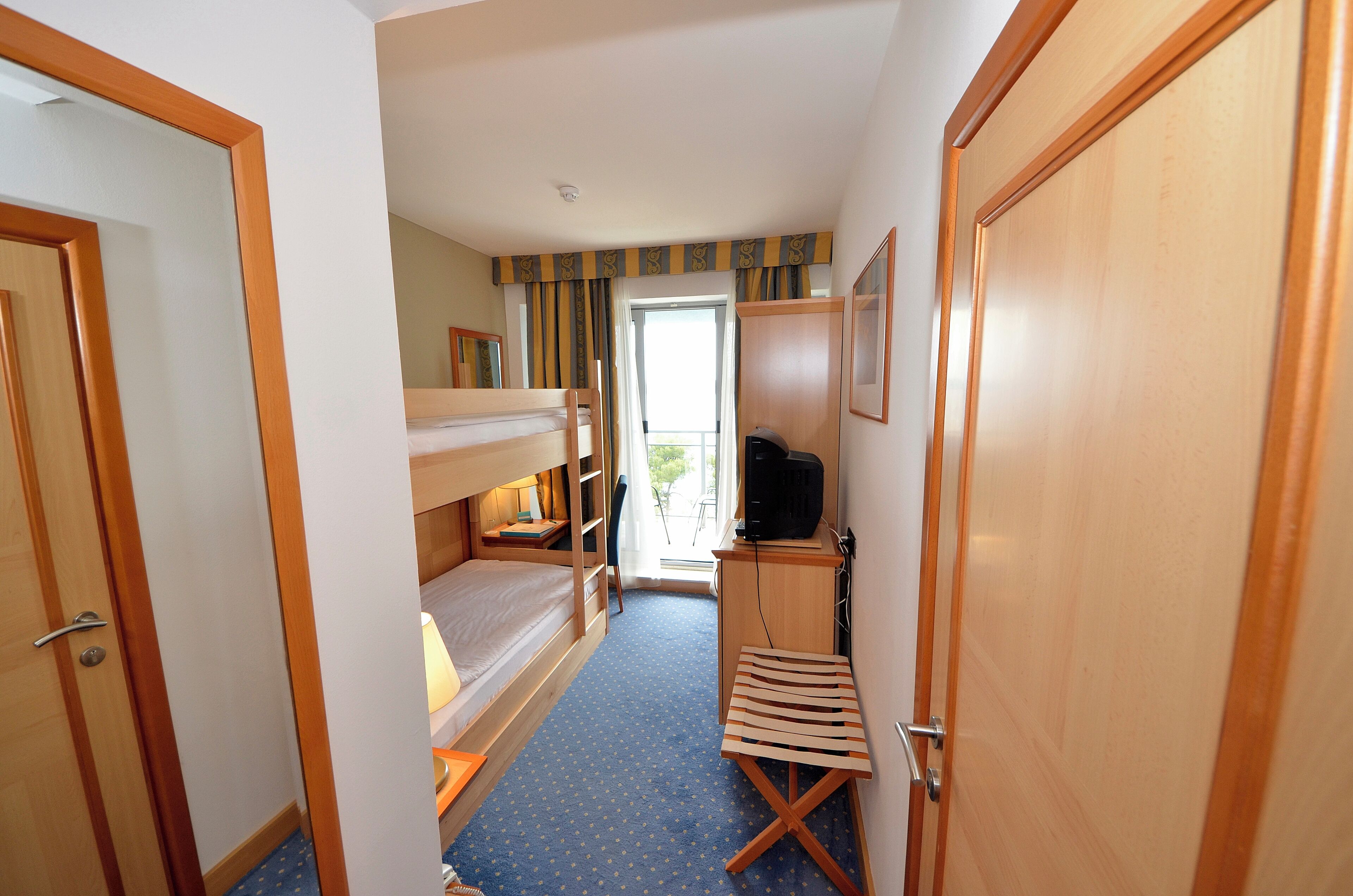 A hotel room with a bunk bed, a desk with a computer, a chair, and a small stool.