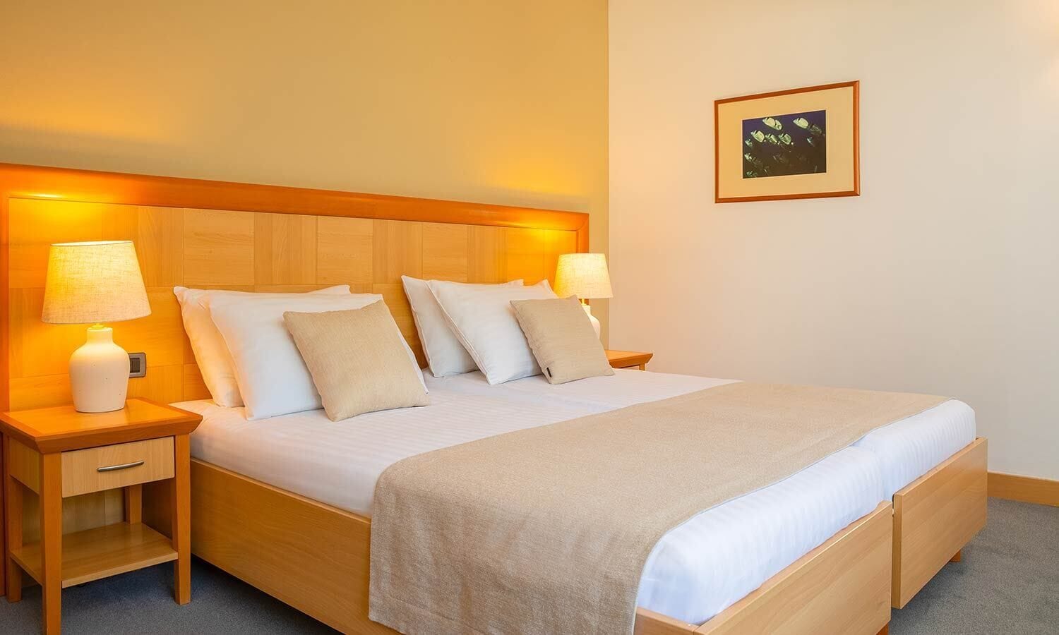A neatly made bed with a wooden headboard, two bedside tables with lamps, and a framed picture on the wall.