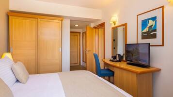 Ein Hotelzimmer mit Bett, Schreibtisch mit Computer, Stuhl, Kleiderschrank und einem gerahmten Bild an der Wand.