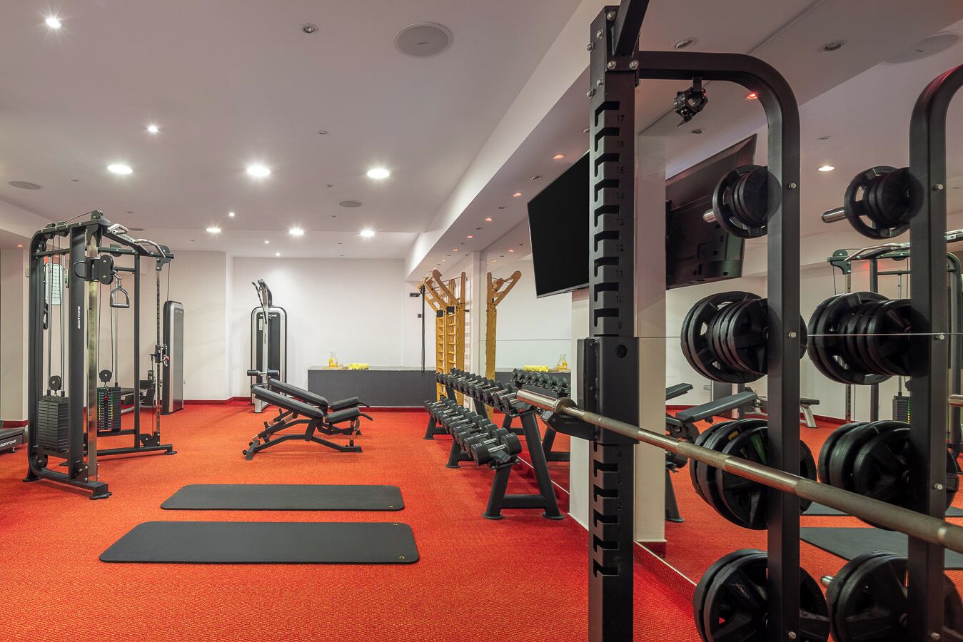 Un gimnasio con equipo de levantamiento de pesas, colchonetas de ejercicio y una banca.