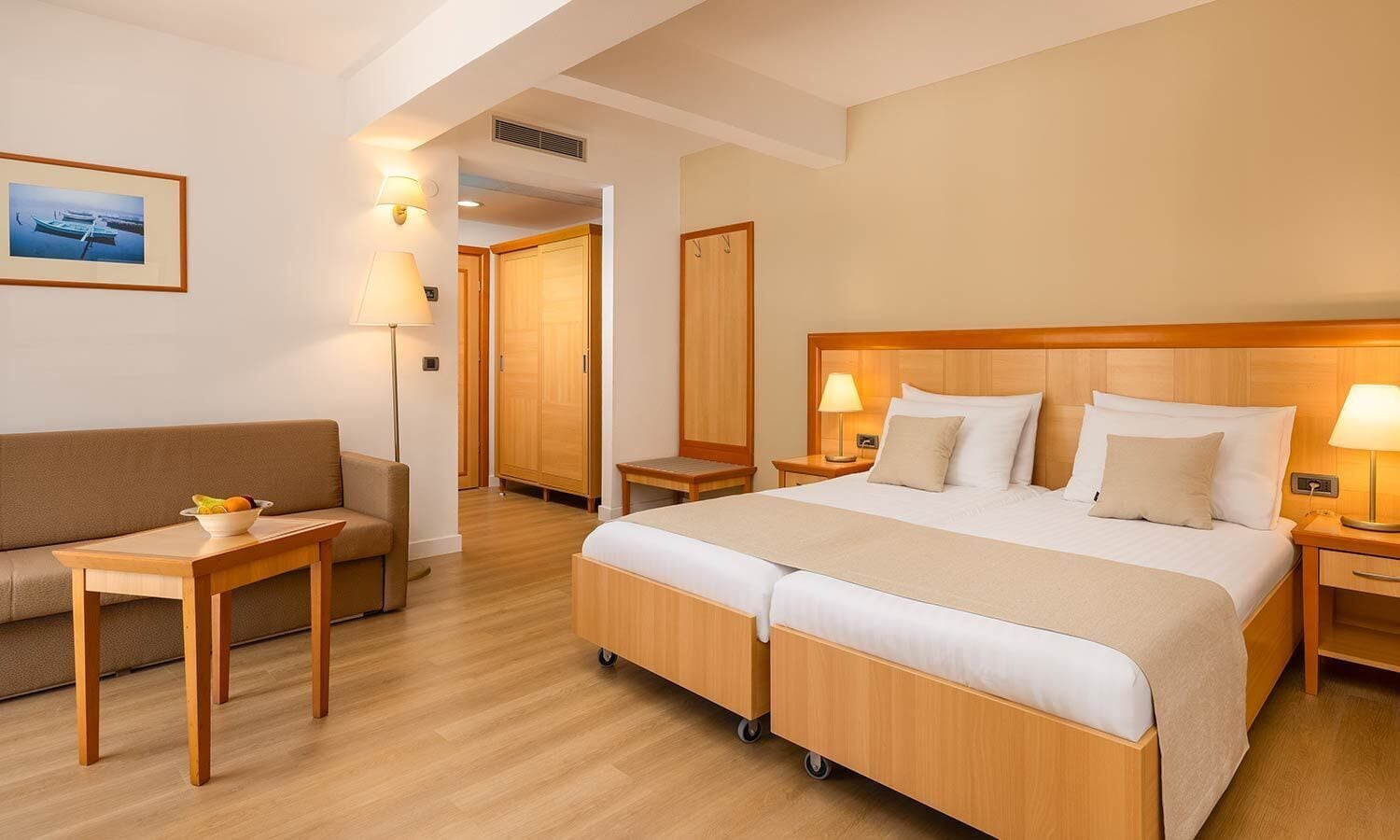 Quarto de hotel com uma cama, um sofá, uma mesinha e uma mesadinha de cabeceira.