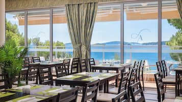 A restaurant with outdoor seating overlooking a body of water, featuring large windows and a view of the landscape.