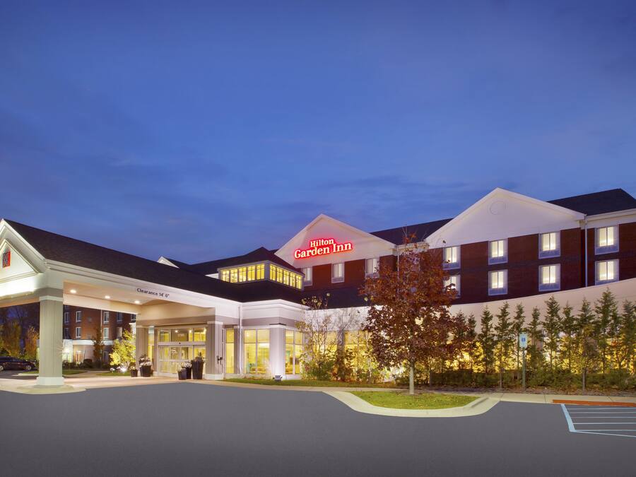 Um hotel com uma placa grande da 'Hilton Garden Inn', entrada coberta e estacionamento.