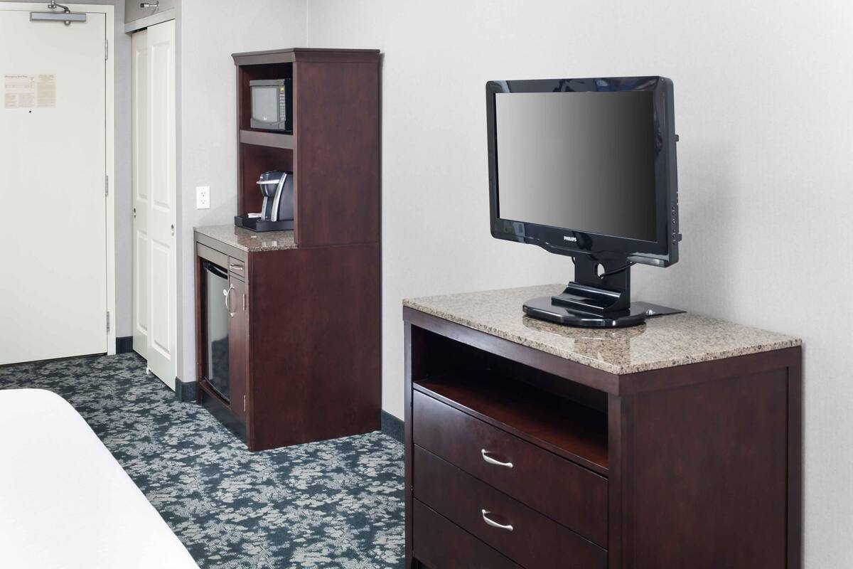 A hotel room with a bed, a TV on a wooden stand, a microwave, and a coffee maker.