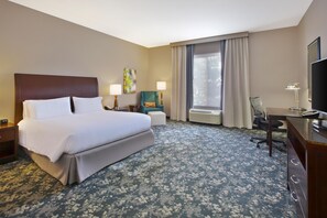 A hotel room with a large bed, a desk, a chair, a TV, and a window with curtains. - Hilton Garden Inn Detroit/Novi (Novi)