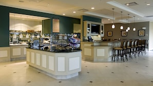 A hotel lobby with a central bar area, seating, and a kitchen visible in the background. - Hilton Garden Inn Detroit/Novi (Novi)