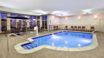 Piscina interna com piso em azulejo, escada para piscina e área de estar com cadeiras e mesas.