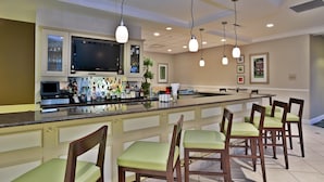A bar area with a long counter, bar stools, a television, and various bottles. - Hilton Garden Inn Detroit/Novi (Novi)