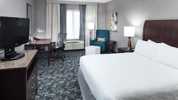A hotel room with a bed, desk, TV, chair, and a window with curtains.