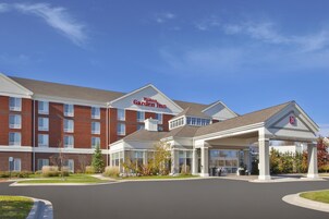 Un Hilton Garden Inn con fachada de ladrillo, entrada cubierta y cielo azul despejado.