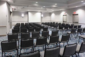 Une salle de conférence avec des rangées de chaises, un écran de projection et une porte de sortie.