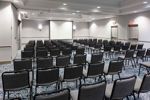 Un salón de conferencias con filas de sillas, una pantalla de proyector y una puerta de salida.