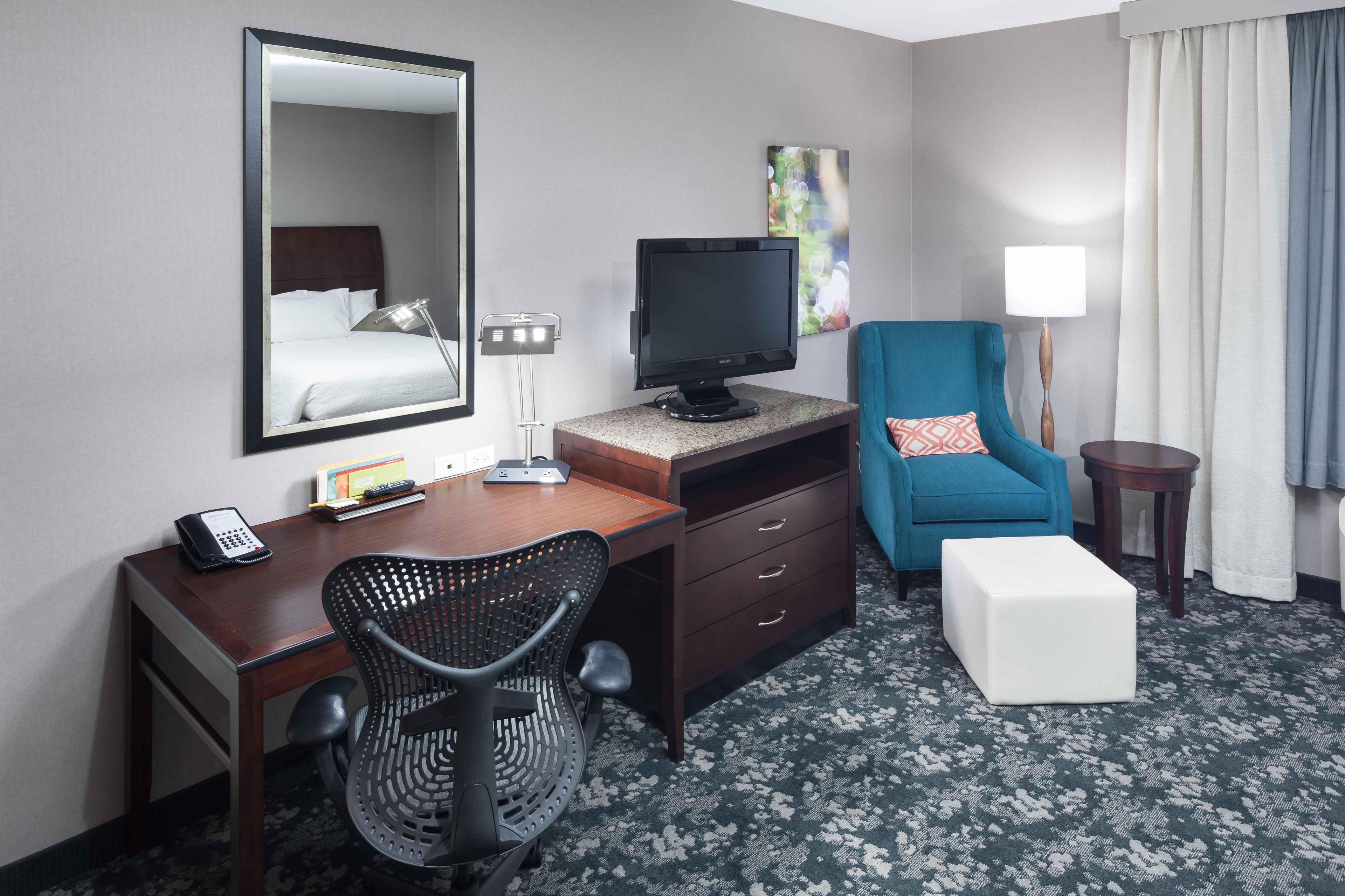 A hotel room with a bed, desk, chair, television, and a small table with a lamp.