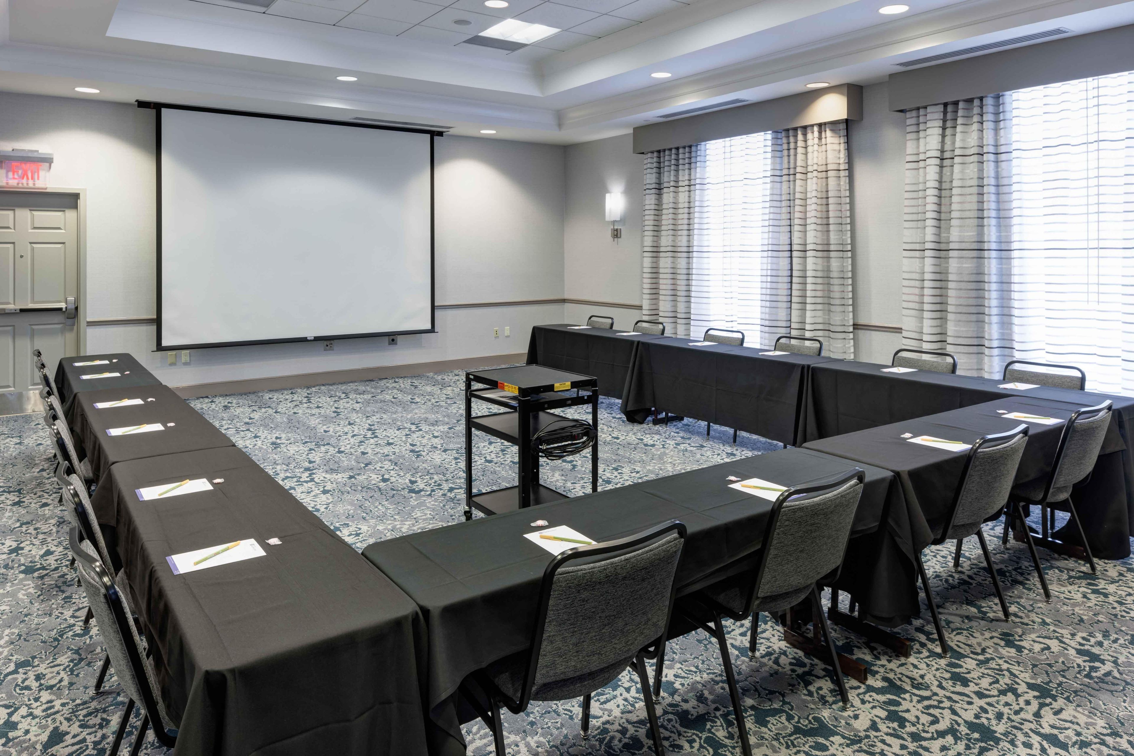 A conference room with a long table, chairs, a projector screen, and a carpeted floor.