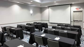 A conference room with tables, chairs, a projector screen, and an exit door.