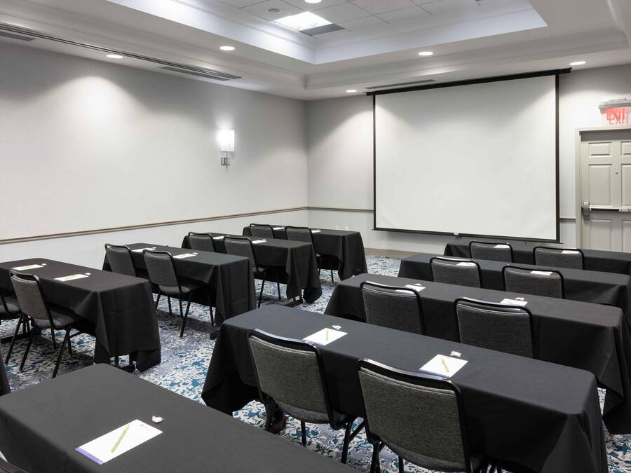 A conference room with tables, chairs, a projector screen, and an exit door.