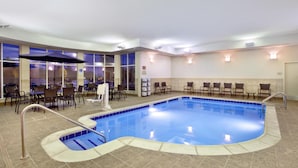 An indoor swimming pool with a tiled floor, a pool ladder, and a seating area with chairs and tables. - Hilton Garden Inn Detroit/Novi (Novi)