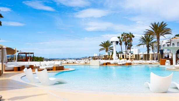 Piscina de un resort con sillas reclinables blancas y palmeras.