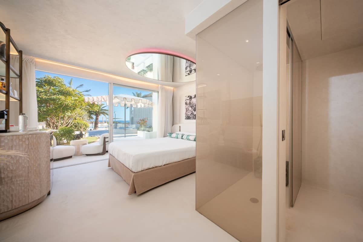A modern bedroom with a large bed, a bathroom with a toilet, and a view of the outdoors.