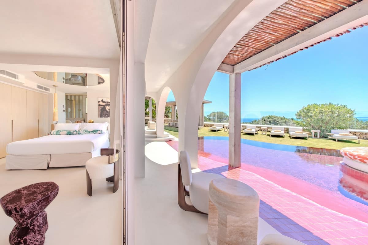 A modern bedroom with a large bed, a bathroom, and a view of a pool and outdoor seating area.