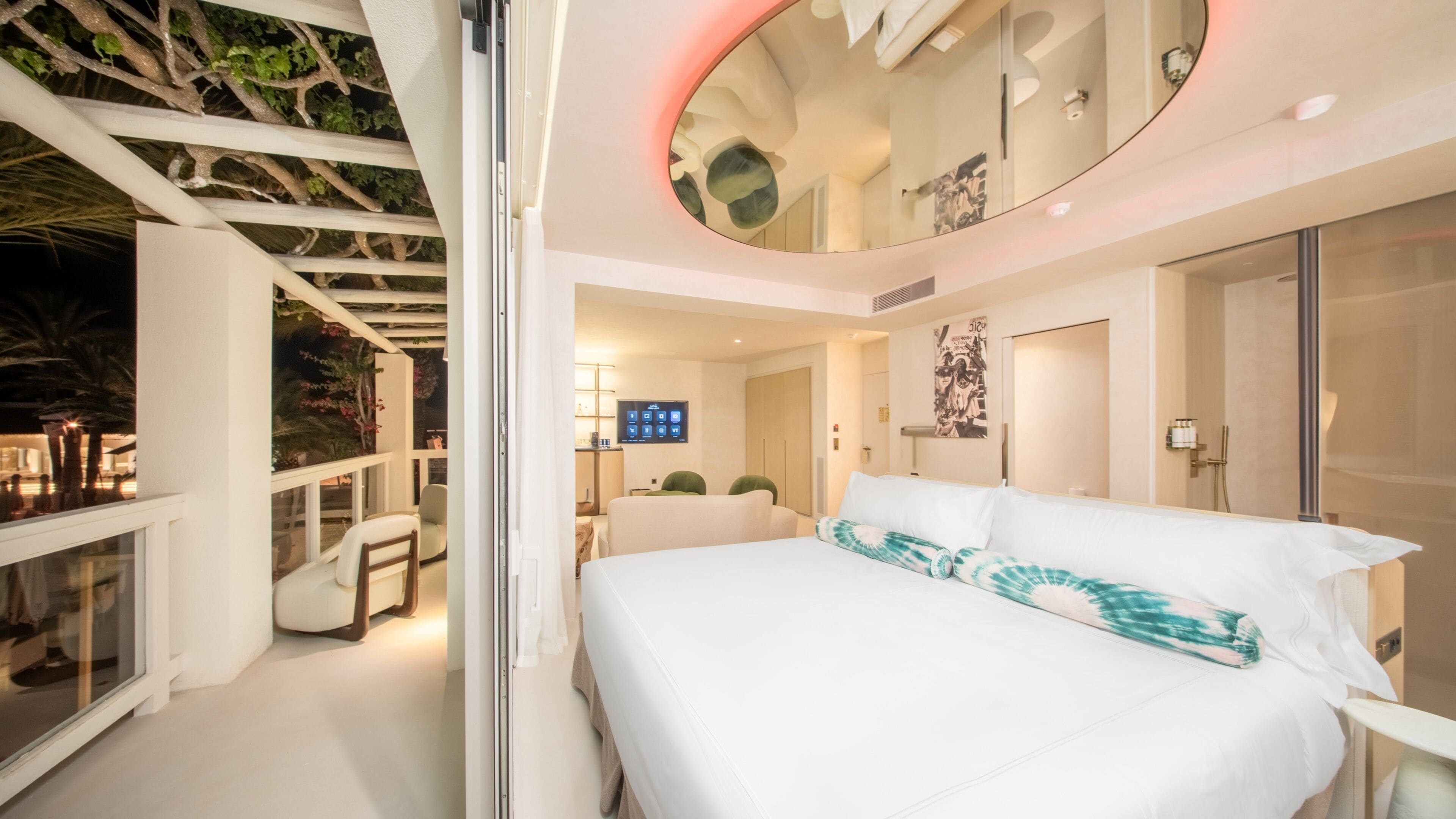 Habitación de hotel moderna con cama, televisión, baño y balcón con plantas.