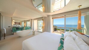 Una habitación de hotel moderna con una cama grande, una bañera, un balcón con vistas al mar y un espejo amplio.