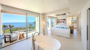 Una habitación de hotel moderna con un ventanal grande, una bañera, una cama y un balcón con vistas al mar.