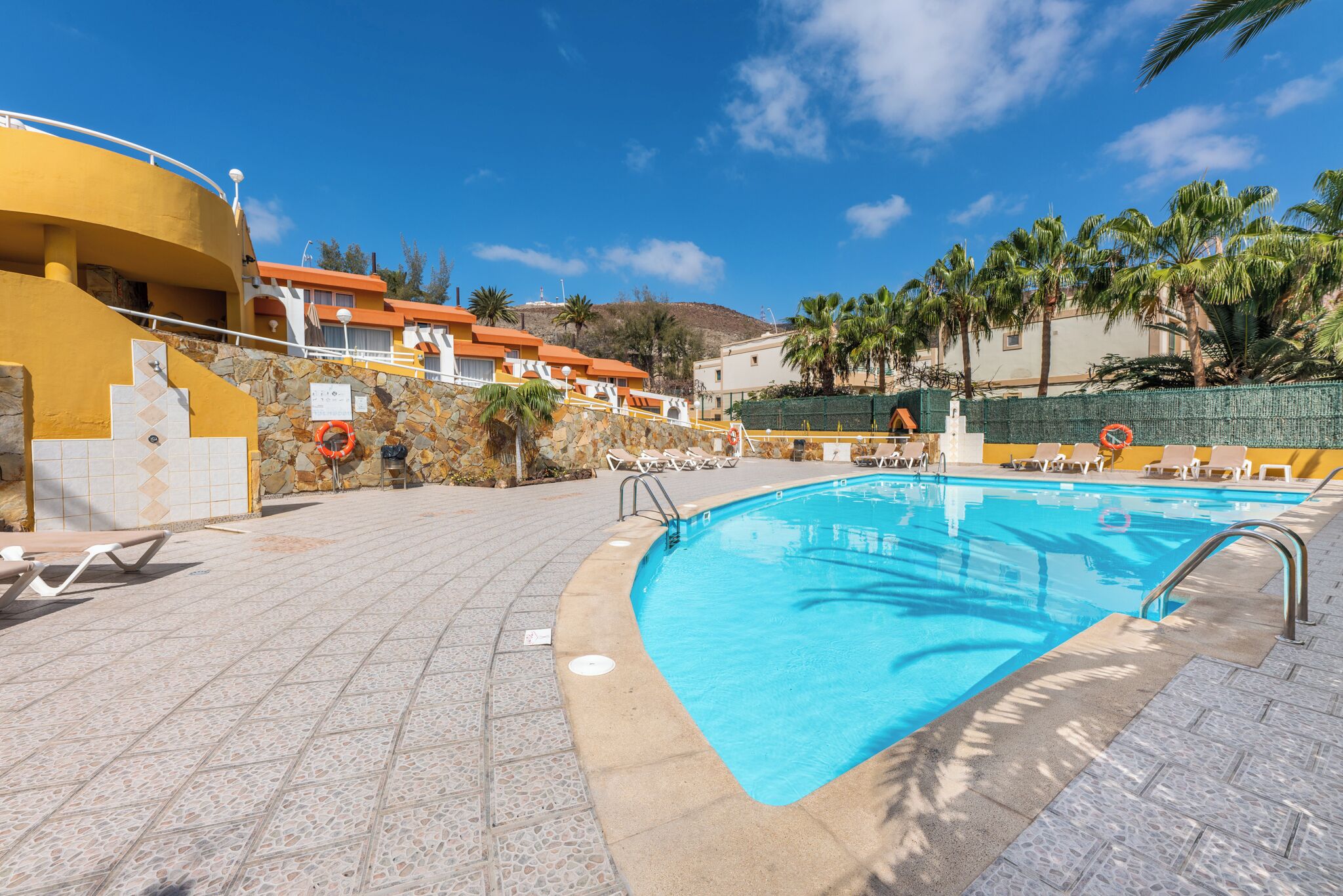 Una piscina con lettini e una parete in pietra.