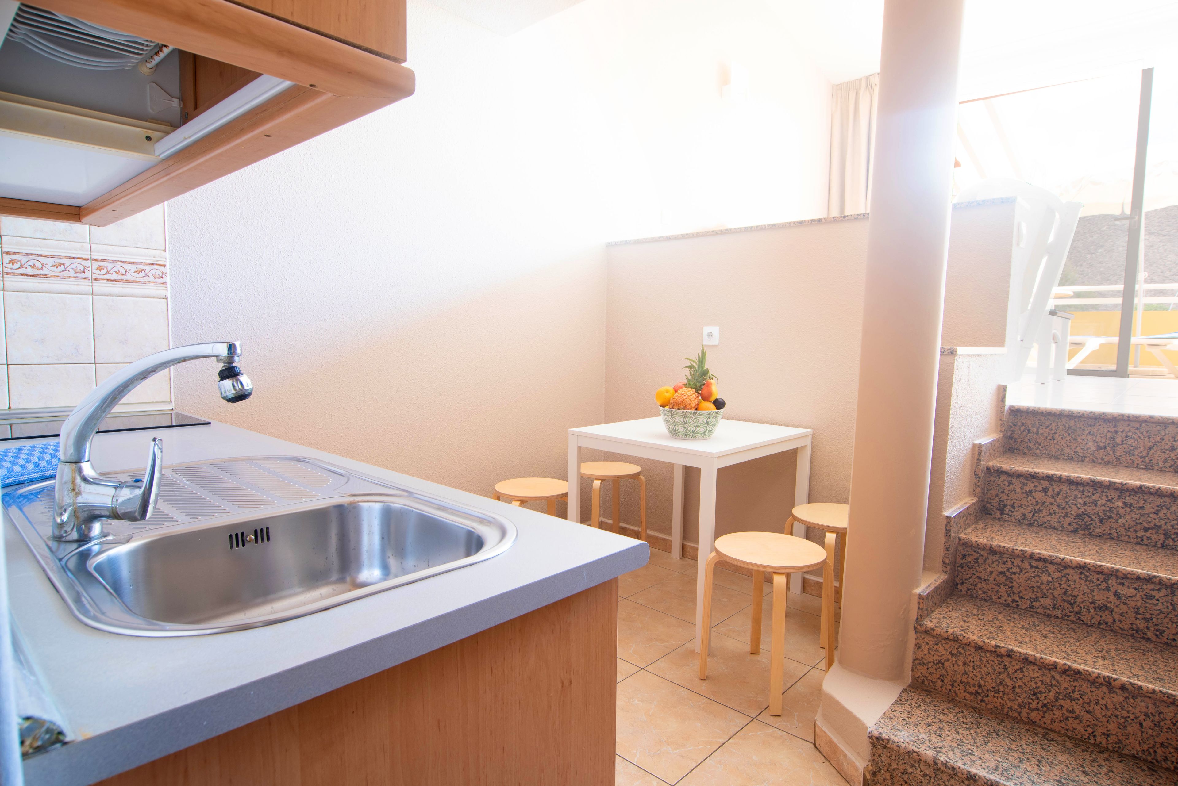 A kitchen with a sink, a small table with chairs, and a staircase leading to an upper level.