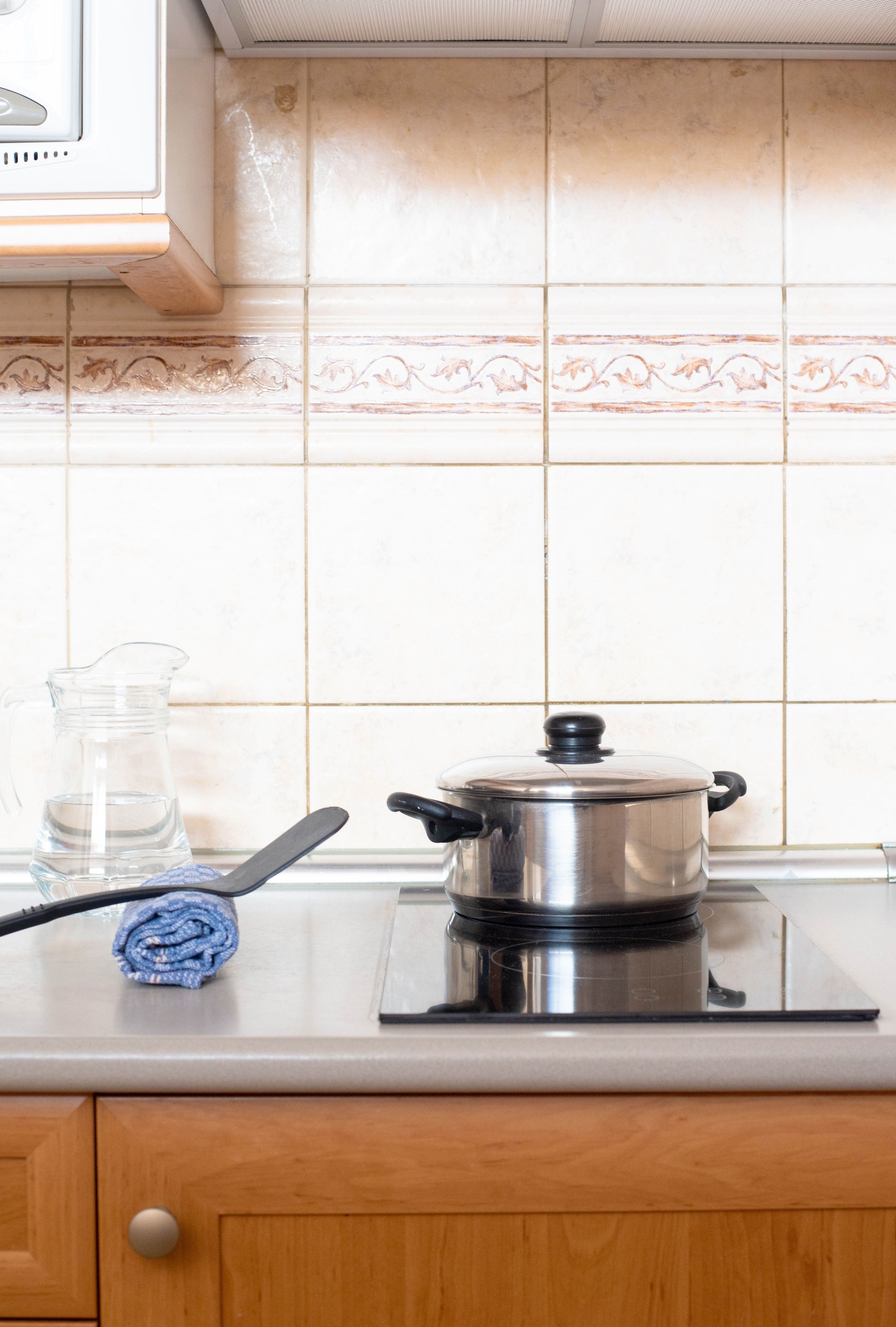 Una cucina con un fornello, una pentola, un boccale di vetro e un asciugamano arrotolato sul piano di lavoro.