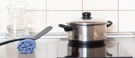 Una cucina con un fornello, una pentola, un boccale di vetro e un asciugamano arrotolato sul piano di lavoro.